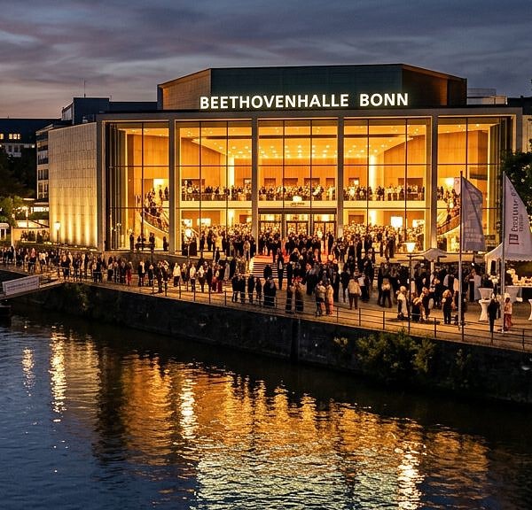 Beethovenhalle in Bonn am Abend: erleuchtete Glasfassade des Konzerthauses, Festivalpublikum auf dem Weg zum Konzert